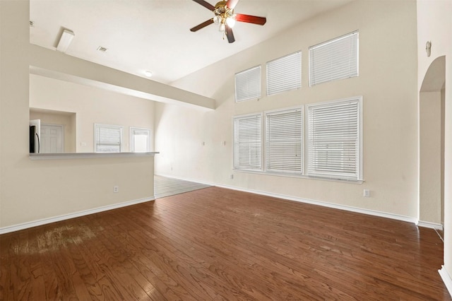 unfurnished living room with baseboards, visible vents, a ceiling fan, arched walkways, and wood finished floors