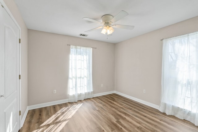 spare room with visible vents, wood finished floors, a ceiling fan, and baseboards