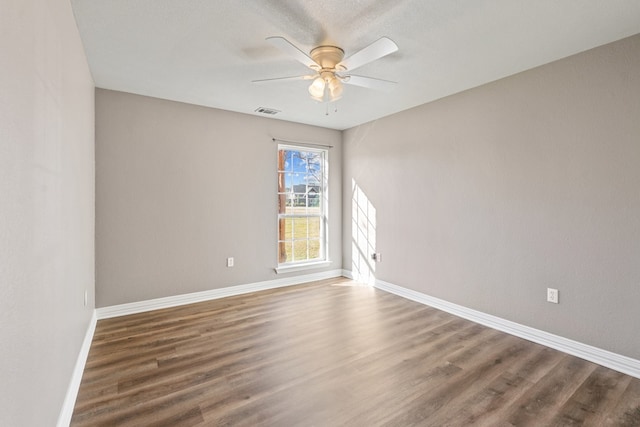 empty room featuring ceiling fan, wood finished floors, visible vents, and baseboards