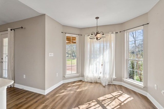 unfurnished dining area with an inviting chandelier, wood finished floors, and baseboards