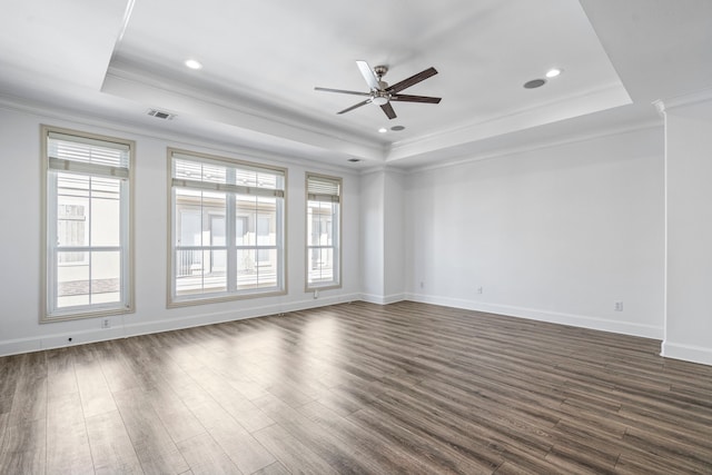 unfurnished room with a tray ceiling, dark wood-style flooring, visible vents, and plenty of natural light