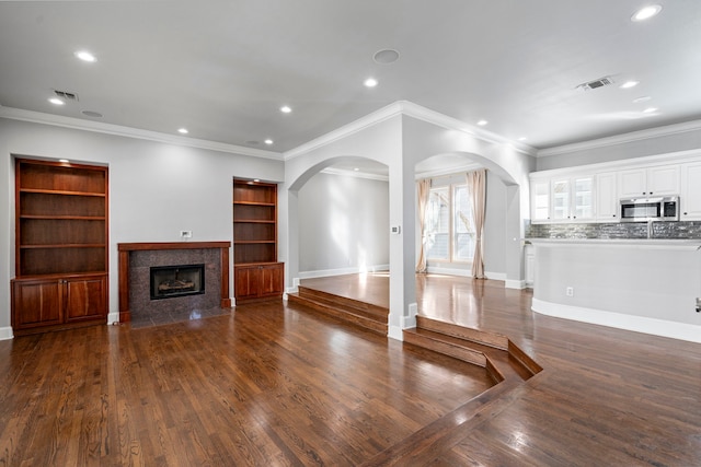 unfurnished living room with a fireplace, visible vents, dark wood finished floors, and arched walkways