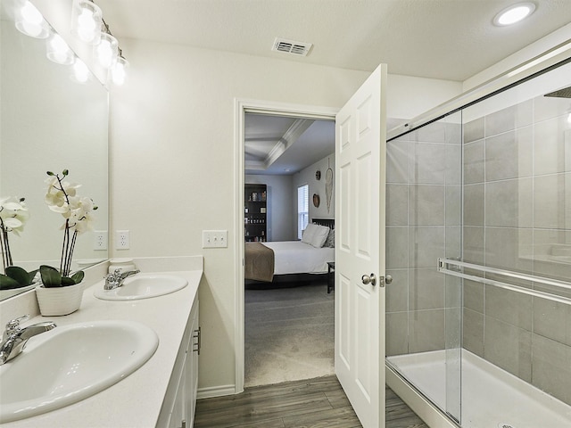 ensuite bathroom featuring a sink, visible vents, wood finished floors, and a shower stall