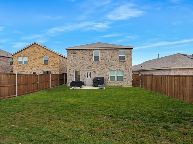 rear view of property with a lawn, a fenced backyard, brick siding, and a patio area