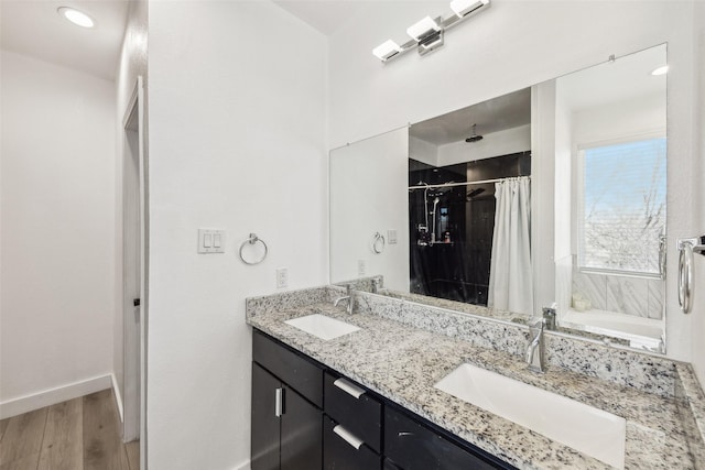 full bathroom featuring double vanity, wood finished floors, a sink, and baseboards