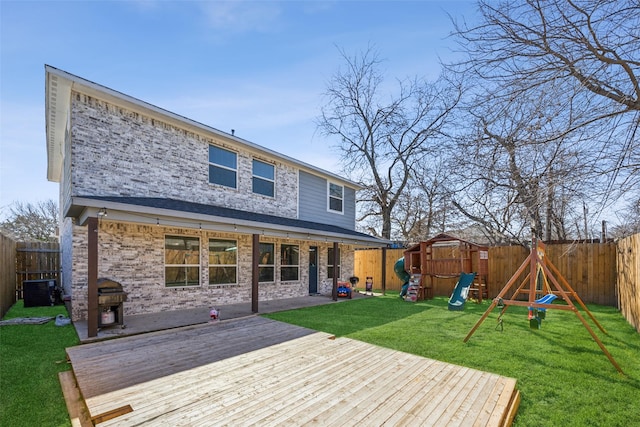 rear view of property with a yard, brick siding, a playground, and a fenced backyard