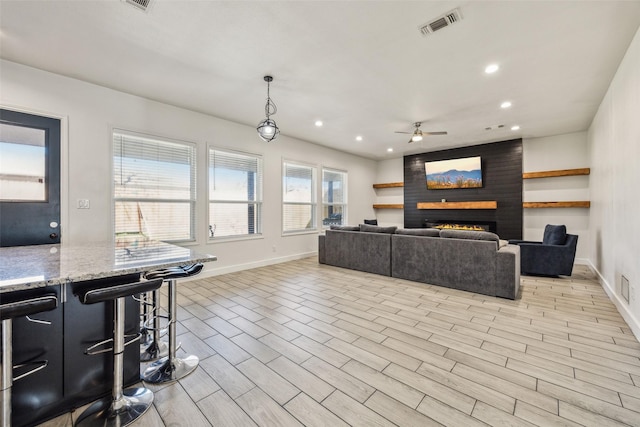 living area featuring baseboards, visible vents, light wood-style floors, a fireplace, and recessed lighting