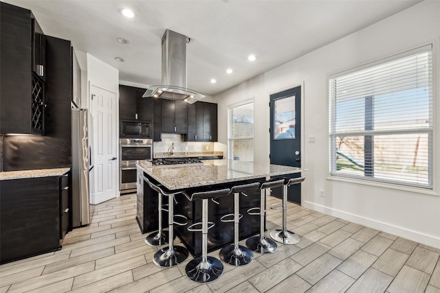 kitchen with stainless steel appliances, wood finish floors, dark cabinetry, and island range hood