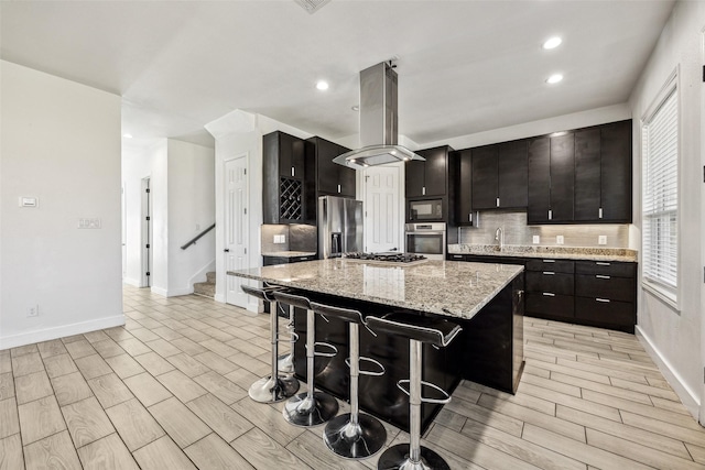 kitchen with wood finish floors, stainless steel appliances, a kitchen island, island range hood, and a kitchen breakfast bar