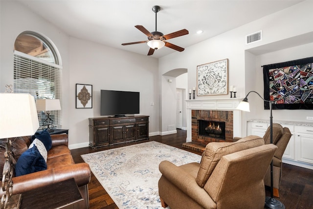 living area with arched walkways, dark wood-style flooring, visible vents, baseboards, and a brick fireplace