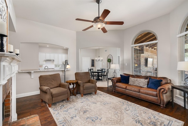 living room featuring visible vents, lofted ceiling, dark wood-style flooring, a brick fireplace, and ceiling fan with notable chandelier