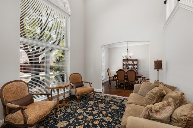 living area with arched walkways, a notable chandelier, a towering ceiling, wood finished floors, and baseboards