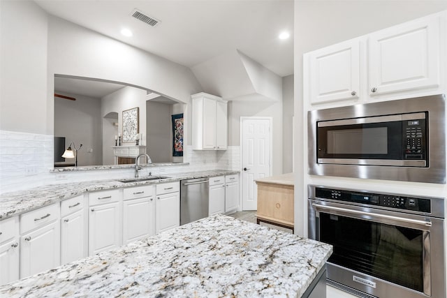 kitchen with light stone counters, stainless steel appliances, a sink, visible vents, and decorative backsplash