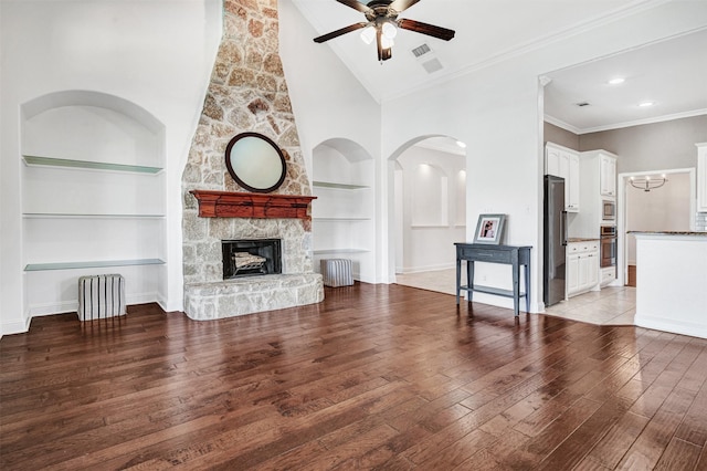 living room featuring ceiling fan, light wood-style flooring, a fireplace, built in features, and crown molding