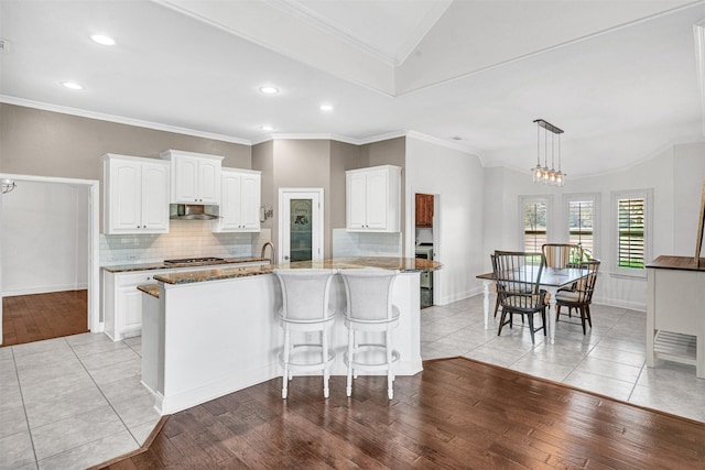 kitchen featuring a chandelier, under cabinet range hood, white cabinets, ornamental molding, and light wood finished floors