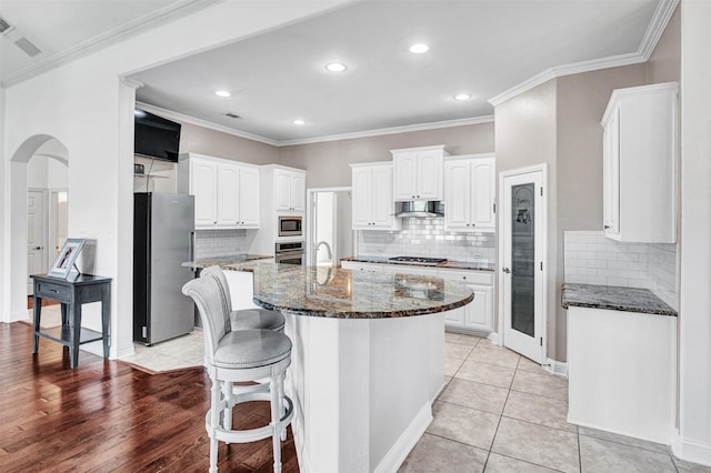 kitchen featuring arched walkways, extractor fan, white cabinets, appliances with stainless steel finishes, and dark stone counters