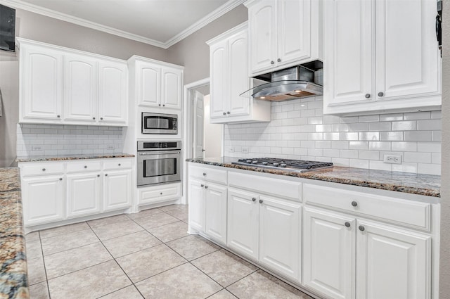 kitchen with under cabinet range hood, appliances with stainless steel finishes, dark stone counters, and crown molding