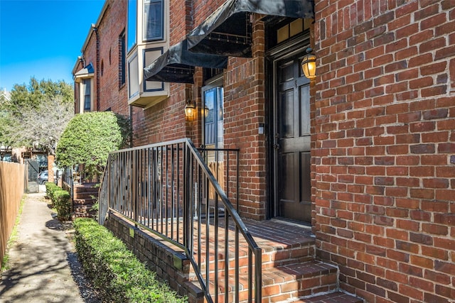 doorway to property featuring brick siding and fence