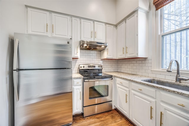 kitchen with decorative backsplash, appliances with stainless steel finishes, white cabinetry, a sink, and exhaust hood