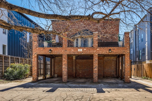 rear view of house featuring driveway, fence, a carport, and brick siding