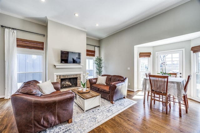 living room with crown molding, a brick fireplace, wood finished floors, and a healthy amount of sunlight