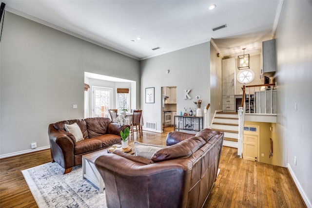 living area featuring ornamental molding, wood finished floors, visible vents, and stairs