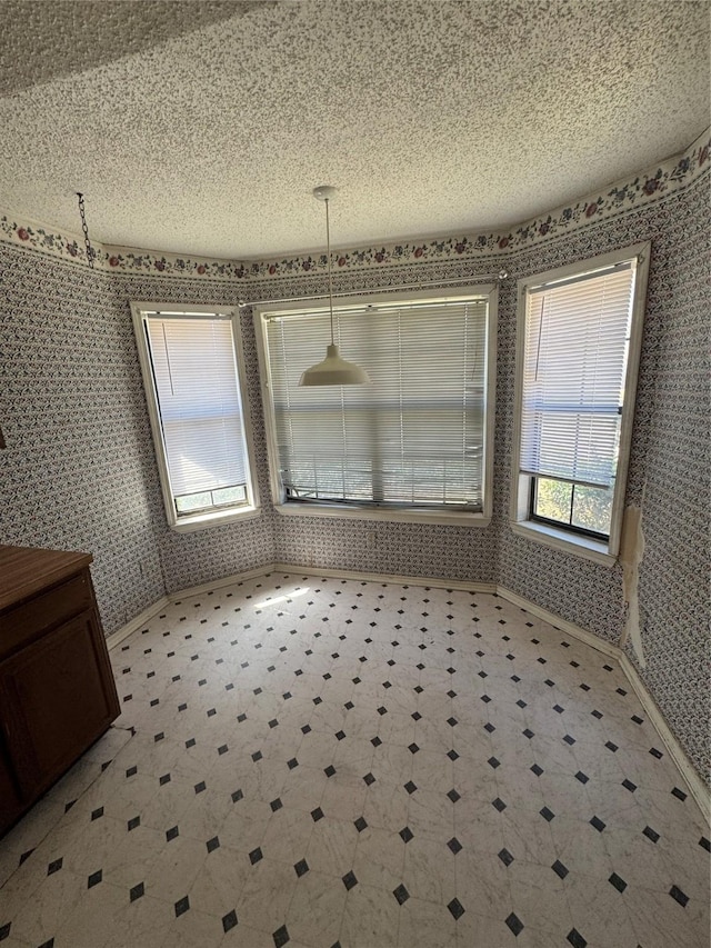 unfurnished dining area featuring a textured ceiling and wallpapered walls