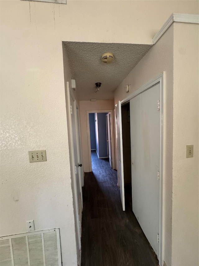 hallway featuring visible vents, a textured ceiling, and wood finished floors