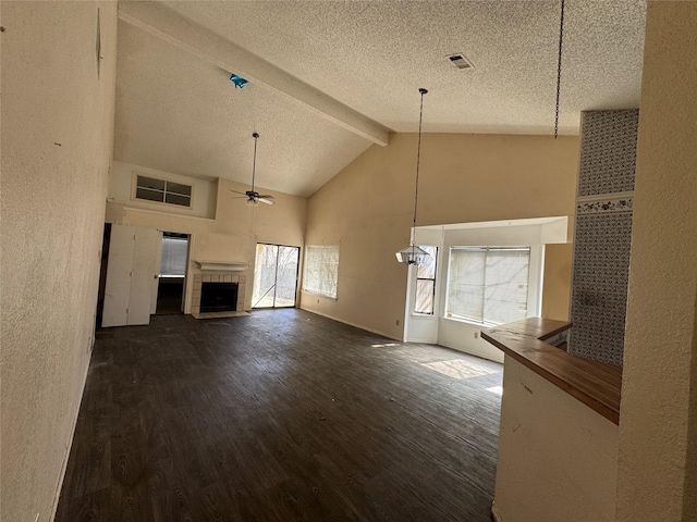 unfurnished living room with ceiling fan, a textured ceiling, dark wood-style flooring, a fireplace, and beam ceiling