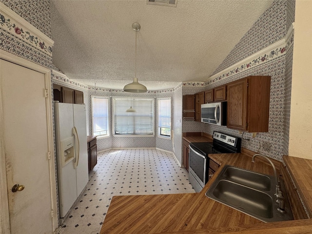 kitchen featuring wallpapered walls, appliances with stainless steel finishes, vaulted ceiling, a textured ceiling, and a sink