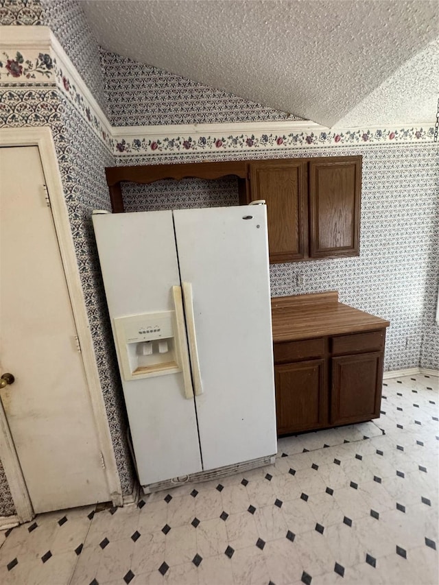 kitchen featuring white fridge with ice dispenser, vaulted ceiling, and wallpapered walls