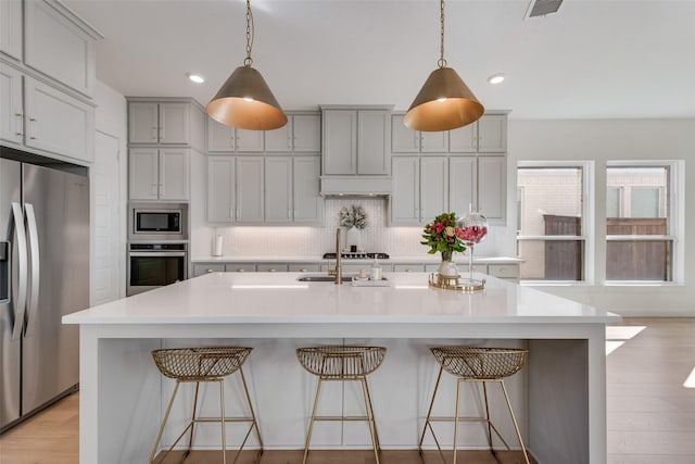 kitchen featuring stainless steel appliances, tasteful backsplash, gray cabinets, light countertops, and light wood-style flooring