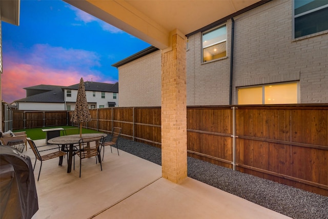 patio terrace at dusk featuring outdoor dining space, a fenced backyard, and grilling area