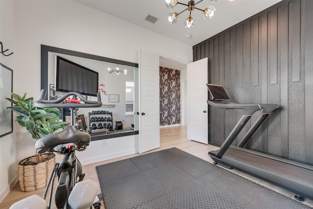 exercise room with baseboards, visible vents, a chandelier, and wood finished floors