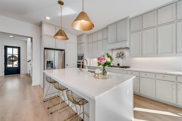 kitchen with tasteful backsplash, appliances with stainless steel finishes, light countertops, light wood-type flooring, and a kitchen bar