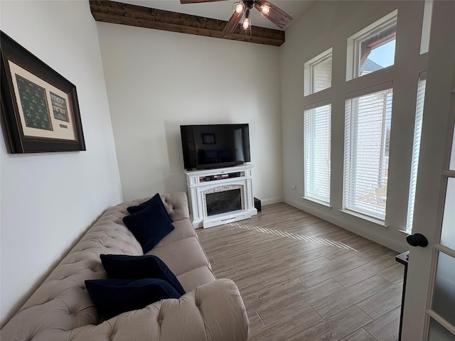 living room with a ceiling fan, a healthy amount of sunlight, beamed ceiling, and wood finished floors