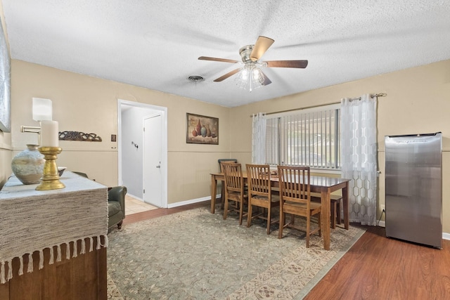 dining room featuring baseboards, visible vents, ceiling fan, wood finished floors, and a textured ceiling