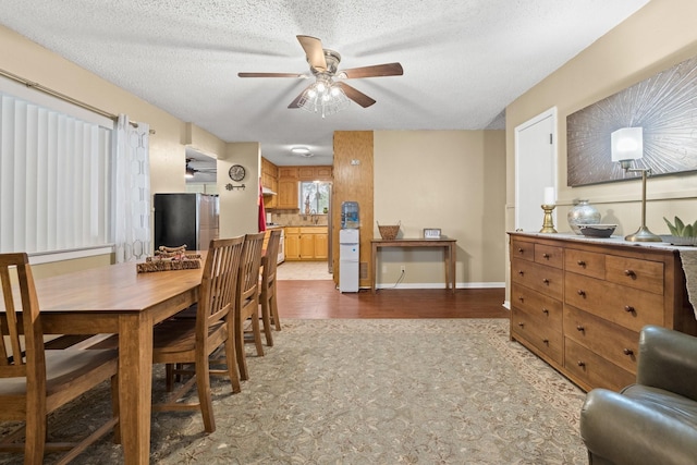 dining room featuring light wood-style floors, a textured ceiling, baseboards, and a ceiling fan