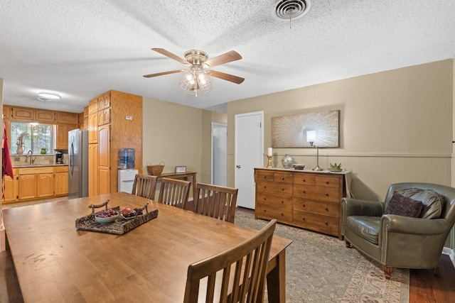 dining area featuring visible vents, a ceiling fan, a wainscoted wall, a textured ceiling, and light wood-style floors