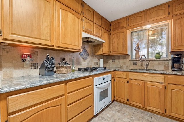 kitchen with light stone counters, white oven, stainless steel gas cooktop, and a sink