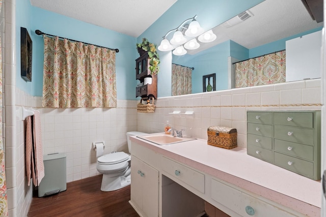 full bath featuring tile walls, visible vents, toilet, a textured ceiling, and wood finished floors