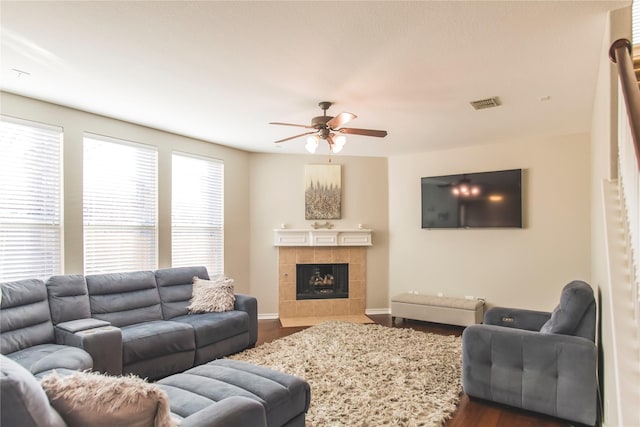 living room with visible vents, baseboards, dark wood finished floors, a tiled fireplace, and a ceiling fan