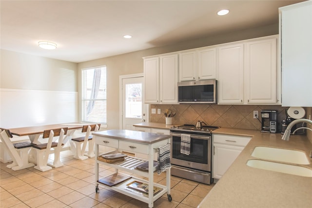 kitchen with backsplash, light countertops, light tile patterned floors, stainless steel appliances, and a sink