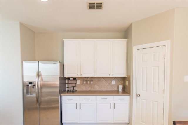 kitchen with visible vents, stainless steel fridge with ice dispenser, light countertops, white cabinetry, and tasteful backsplash