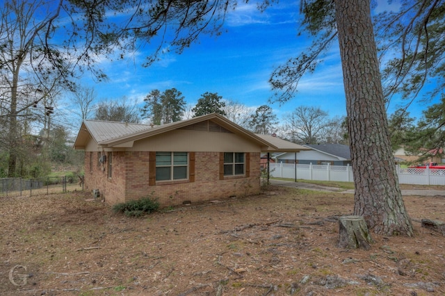 view of property exterior with brick siding, metal roof, fence, and a carport