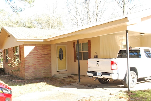 view of front of home with entry steps, metal roof, a carport, and brick siding