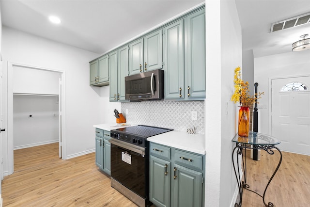 kitchen featuring light wood-type flooring, range with electric cooktop, stainless steel microwave, and backsplash