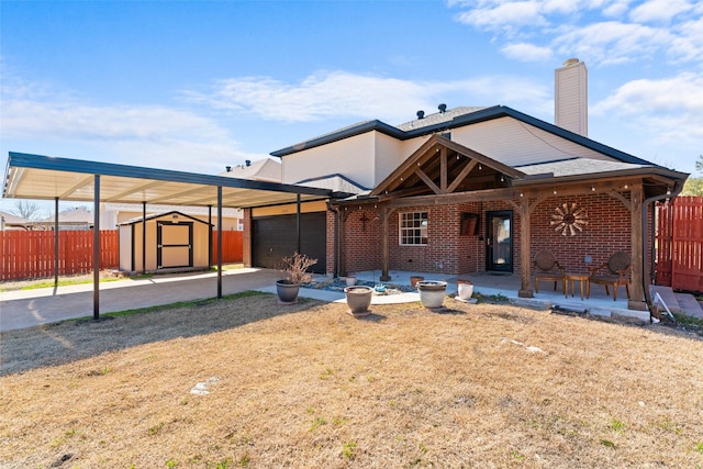 back of house featuring brick siding, a storage unit, fence, a carport, and driveway