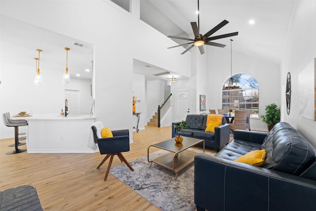 living room with a towering ceiling, light wood-style floors, stairs, and visible vents