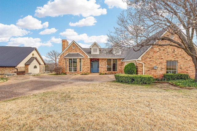 view of front facade with a shingled roof, a front yard, a chimney, and brick siding